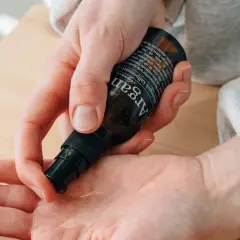 En hand pumpar ut arganolja ansikte ur en mörk flaska. Oljan är ekologisk och kallpressad.