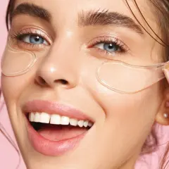 En kvinna med blå ögon och ett leende visar hur ska eye patches sitta under ögonen för en fräsch look.