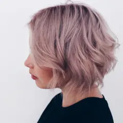 En kvinna med lockigt kort hår i en mjuk roséguld nyans, stylat med volym och textur.