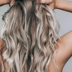 En person med blont, vågigt hår som håller om nacken. Håret ser ut att vara blekt med citron för en naturlig solkysst look.