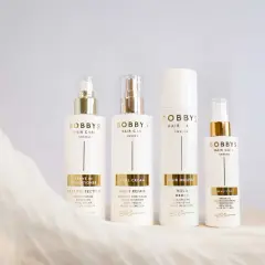 Fyra vita flaskor från Bobby's Hair Care med gulddetaljer. Produkterna hjälper mot statiskt hår och ger glans.