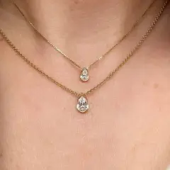Två guldhalsband med päronformade diamanter, ett elegant val av moderna smycken som framhäver halsens linjer.