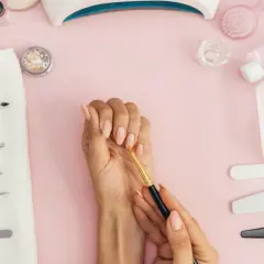 En hand med fina naglar med blommor-mönster, omgiven av manikyrverktyg och nagellack.