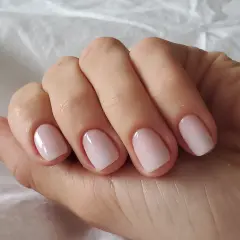 En hand med perfektionerad nagelbandsvård, en klassisk russian manicure med ljusrosa naglar som glänser.