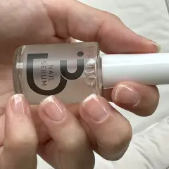 En hand håller en flaska nagelserum. Naglarna är naturliga och visar tecken på att de skivar sig, men serumet kan hjälpa till att stärka dem.