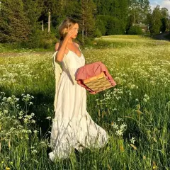 En kvinna i vita klänningar går genom en blomsteräng med en picknickkorg.