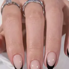 Ett par händer med eleganta press on nails i fransk manikyr med svarta spetsar. Två ringar pryder fingrarna.