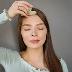 En kvinna med slutna ögon använder en gua sha för ansiktet, en del av hennes skönhetsrutin.