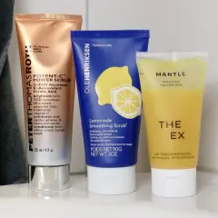 Tre tuber med ansiktsskrubb: en kopparfärgad, en blå med citron och en gul. Dessa produkter erbjuder mekanisk peeling för huden.