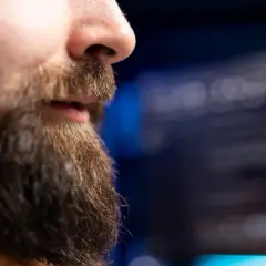 En närbild på en mans ansikte med skägg och en rak mustasch. Bakgrunden är suddig och mörk.