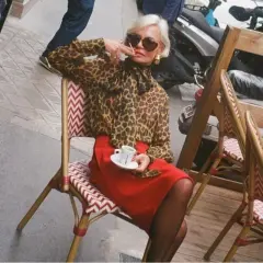 Elegant dam i leopardmönstrad blus och röd kjol, en kaffe i handen. En stil som inspirerar för vårmode 2026 dam.