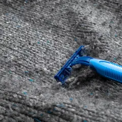En blå rakhyvel ligger på en grå stickad tröja, redo att ta bort noppor.