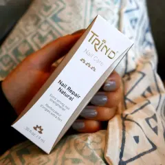 En hand håller en Trind Nail Repair Natural-förpackning. Produkten är inte farlig, utan en nagelförstärkare.