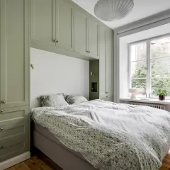 Sovrum med gröna garderober som ramar in sängen. Sängkläder med blommigt mönster. Ett fönster med utsikt över trädgård. Ett objekt rea som passar perfekt.