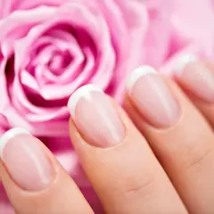 Vackra franska manikyrnaglar framför en mjuk rosa ros. Perfekt för att fila ner tjocka naglar och få en elegant look.