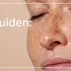 En närbild av en kvinna med fräknar som får en kräm med glykolsyra på kinden. Texten "Ingrediensguiden: Glykolsyra" syns tydligt.