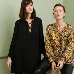 Två kvinnor poserar i en studio. Den ena bär en svart klänning med snörning, den andra en blus med leopardmönster. Båda utstrålar en elegant fransk stil.