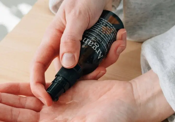 En hand pumpar ut arganolja ansikte ur en mörk flaska. Oljan är ekologisk och kallpressad.