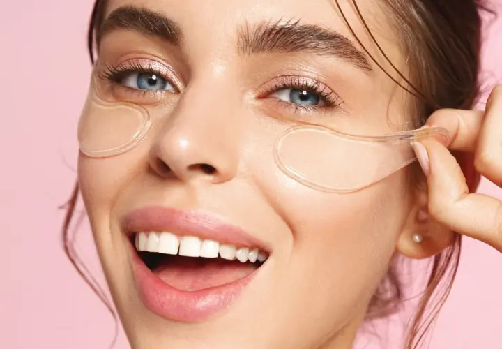 En kvinna med blå ögon och ett leende visar hur ska eye patches sitta under ögonen för en fräsch look.