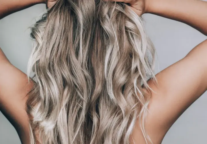 En person med blont, vågigt hår som håller om nacken. Håret ser ut att vara blekt med citron för en naturlig solkysst look.