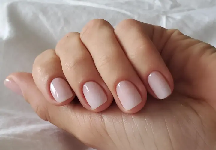 En hand med perfektionerad nagelbandsvård, en klassisk russian manicure med ljusrosa naglar som glänser.