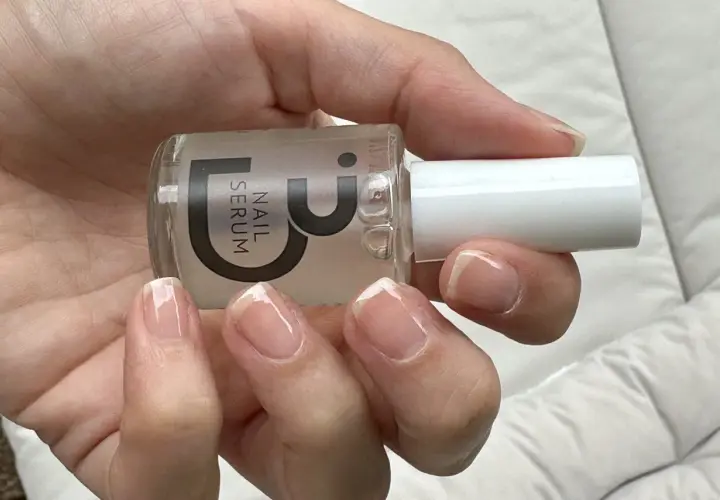 En hand håller en flaska nagelserum. Naglarna är naturliga och visar tecken på att de skivar sig, men serumet kan hjälpa till att stärka dem.