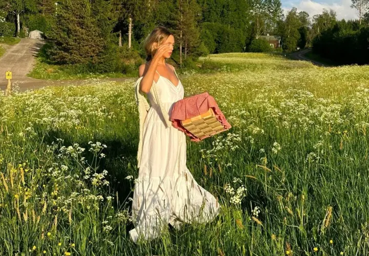 En kvinna i vita klänningar går genom en blomsteräng med en picknickkorg.