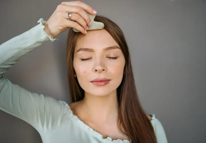 En kvinna med slutna ögon använder en gua sha för ansiktet, en del av hennes skönhetsrutin.