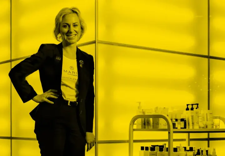 Maria Åkerberg, med en t-shirt med hennes namn, står stolt bredvid en hylla med hudvårdsprodukter.