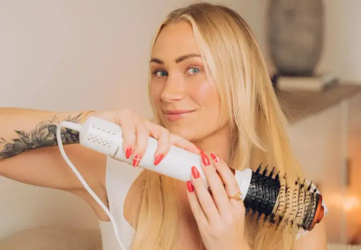 Blond kvinna med tatuering på armen använder en stylingborste för att skapa en perfekt blowout.