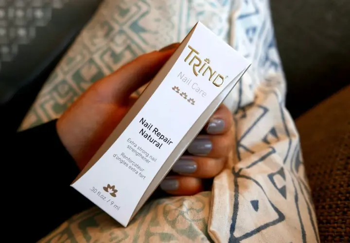 En hand håller en Trind Nail Repair Natural-förpackning. Produkten är inte farlig, utan en nagelförstärkare.