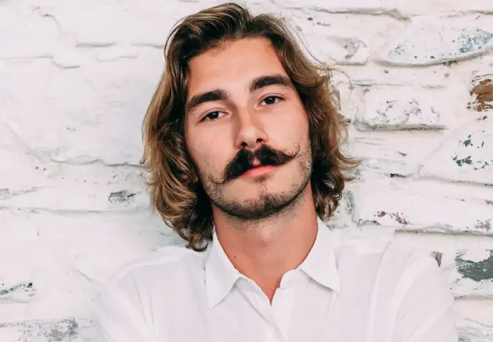 Ung man med långt hår och en imponerande mustasch som visar upp olika mustasch stilar.
