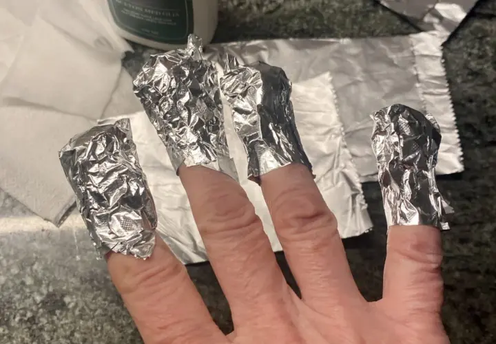 Fingrar inslagna i folie för att ta bort gellack hemma.