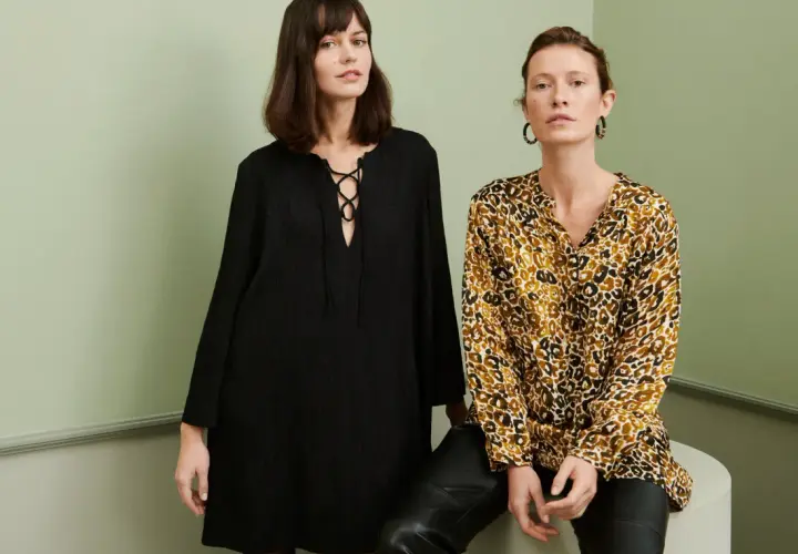 Två kvinnor poserar i en studio. Den ena bär en svart klänning med snörning, den andra en blus med leopardmönster. Båda utstrålar en elegant fransk stil.