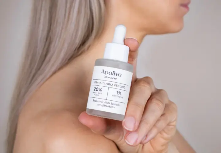En hand håller en flaska med Apoliva PHA+AHA+BHA Peeling. Denna aha syra-produkt hjälper till att reducera döda hudceller.