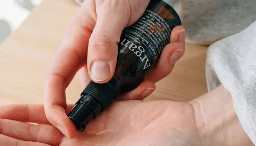 En hand pumpar ut arganolja ansikte ur en mörk flaska. Oljan är ekologisk och kallpressad.