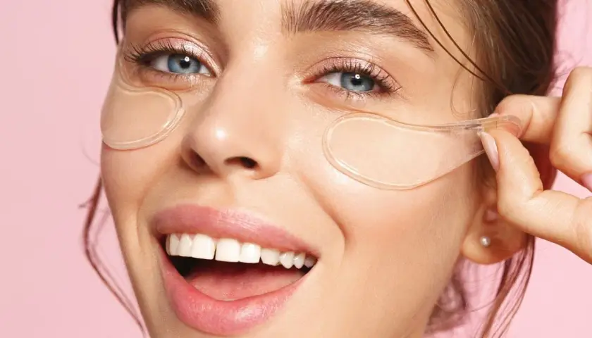 En kvinna med blå ögon och ett leende visar hur ska eye patches sitta under ögonen för en fräsch look.