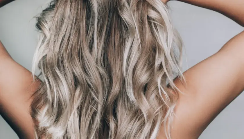 En person med blont, vågigt hår som håller om nacken. Håret ser ut att vara blekt med citron för en naturlig solkysst look.