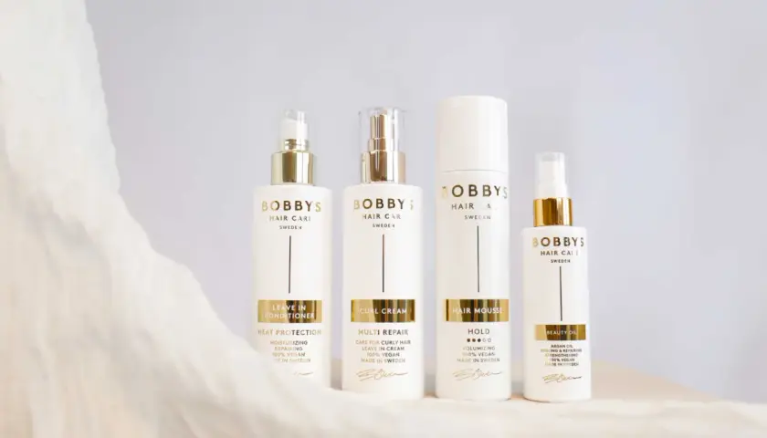 Fyra vita flaskor från Bobby's Hair Care med gulddetaljer. Produkterna hjälper mot statiskt hår och ger glans.