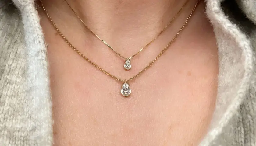 Två guldhalsband med päronformade diamanter, ett elegant val av moderna smycken som framhäver halsens linjer.