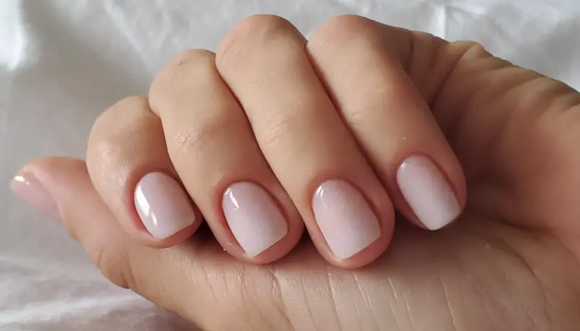 En hand med perfektionerad nagelbandsvård, en klassisk russian manicure med ljusrosa naglar som glänser.
