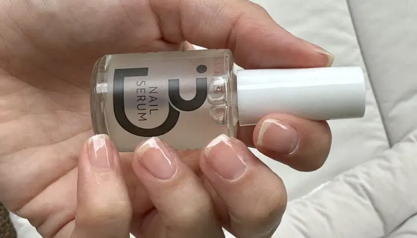 En hand håller en flaska nagelserum. Naglarna är naturliga och visar tecken på att de skivar sig, men serumet kan hjälpa till att stärka dem.