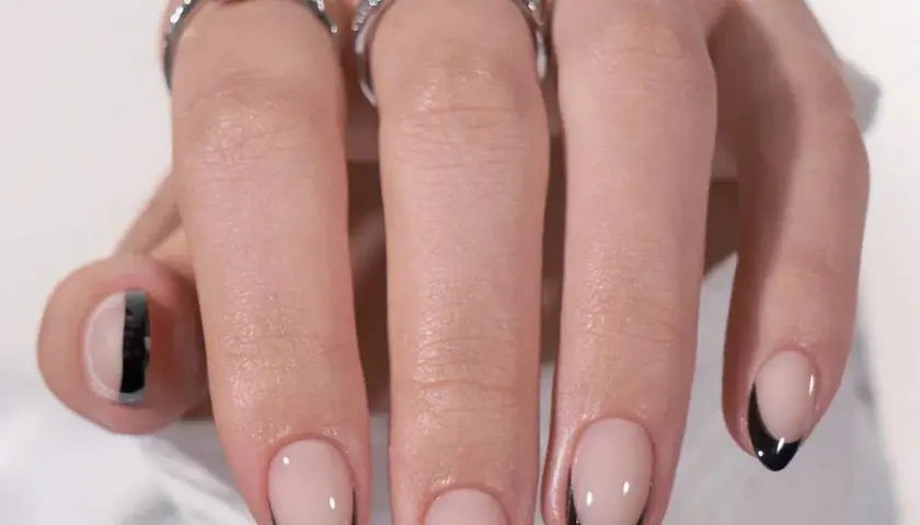 Ett par händer med eleganta press on nails i fransk manikyr med svarta spetsar. Två ringar pryder fingrarna.