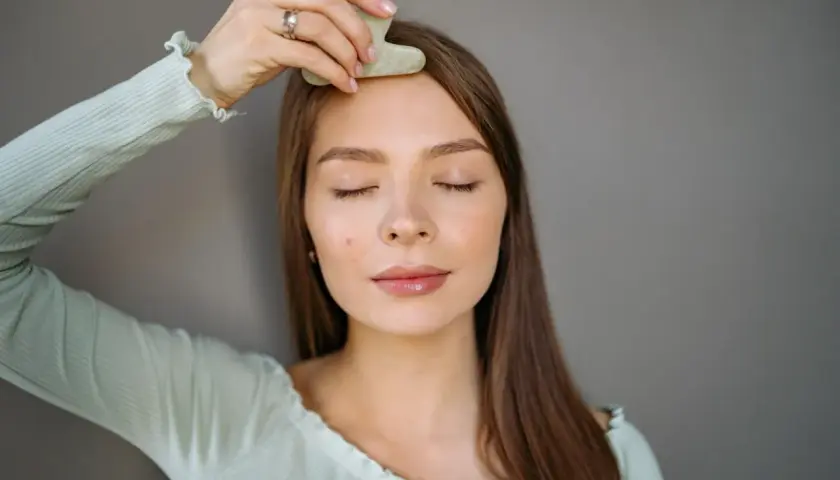 En kvinna med slutna ögon använder en gua sha för ansiktet, en del av hennes skönhetsrutin.