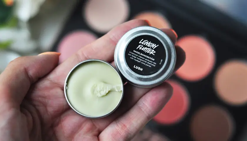En hand håller en burk med Lemony Flutter nagelbands-kräm, perfekt för torra nagelband.