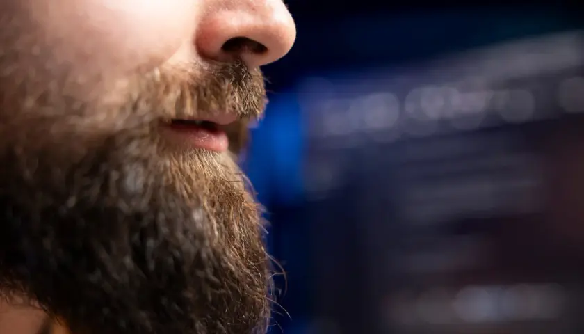 En närbild på en mans ansikte med skägg och en rak mustasch. Bakgrunden är suddig och mörk.
