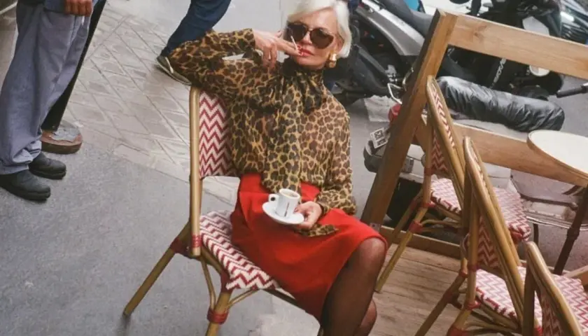 Elegant dam i leopardmönstrad blus och röd kjol, en kaffe i handen. En stil som inspirerar för vårmode 2026 dam.