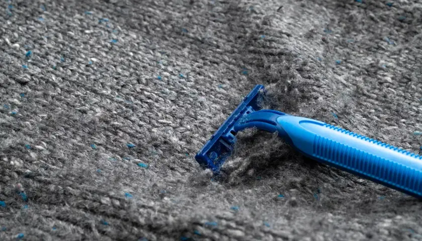 En blå rakhyvel ligger på en grå stickad tröja, redo att ta bort noppor.