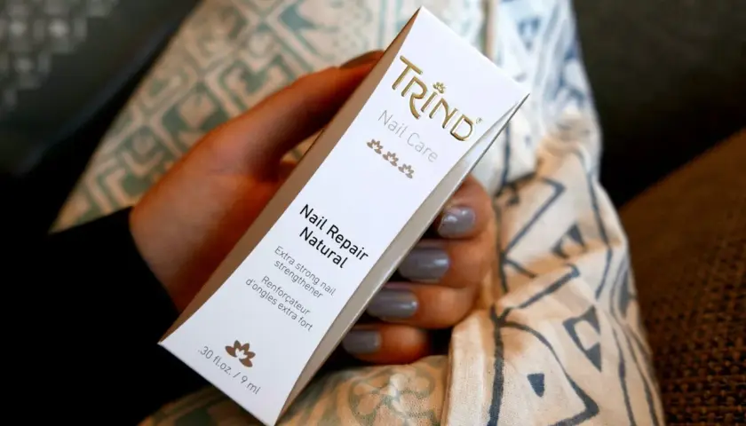 En hand håller en Trind Nail Repair Natural-förpackning. Produkten är inte farlig, utan en nagelförstärkare.