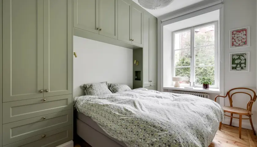 Sovrum med gröna garderober som ramar in sängen. Sängkläder med blommigt mönster. Ett fönster med utsikt över trädgård. Ett objekt rea som passar perfekt.
